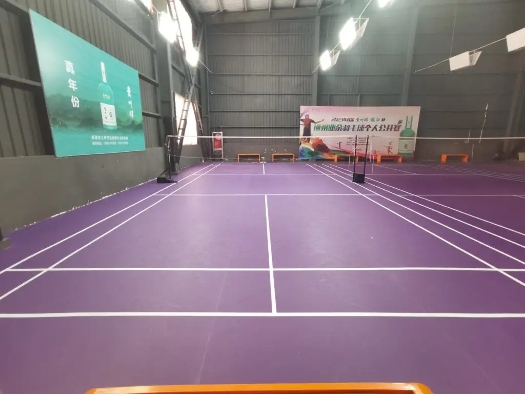 Cancha de badminton con piso púrpura y publicidad
